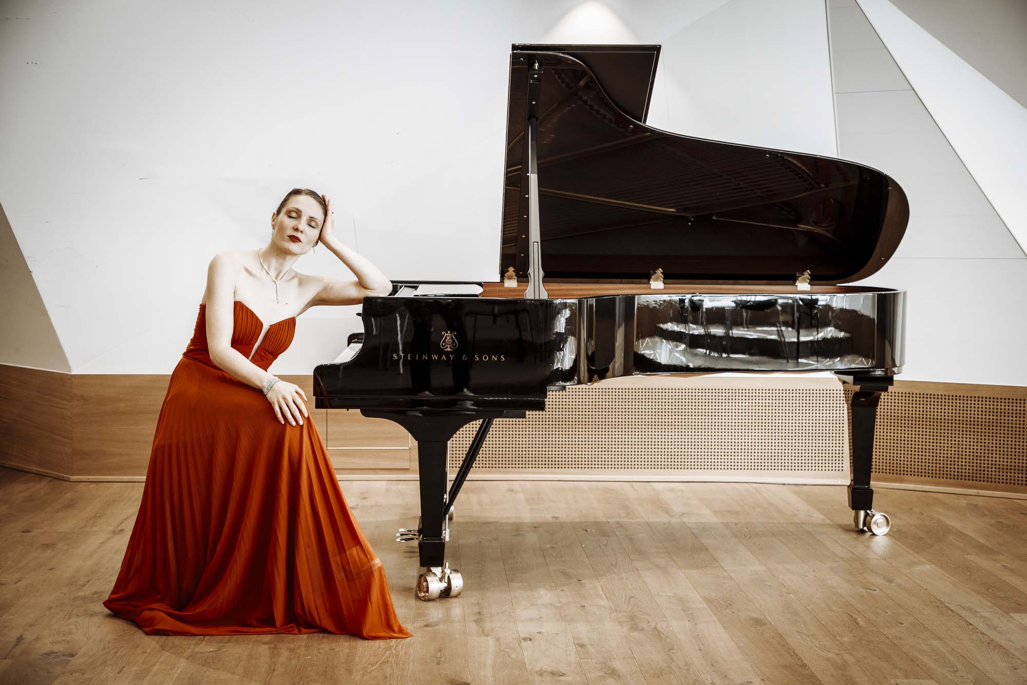 Nicole Tschaikin im roten Konzertkleid neben einem Steinway Flügel