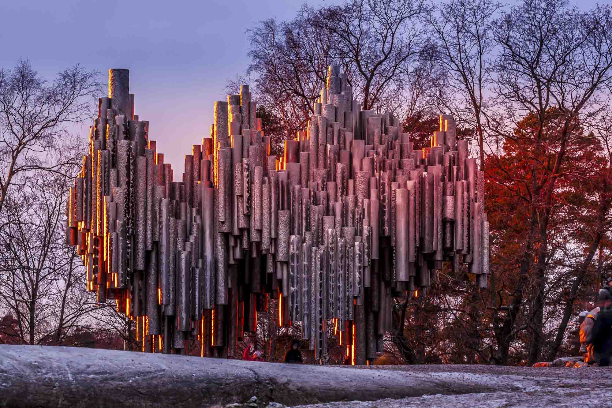 Die silbernen Röhren des Sibelius-Denkmals im warmen Abendlicht, umgeben von Bäumen und Schnee